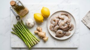 Fresh raw shrimp, green asparagus, garlic, and lemons on a marble countertop.