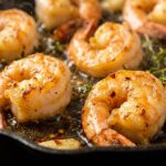 Searing jumbo shrimp to a golden brown in a hot pan with olive oil.